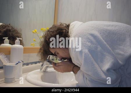 Un jeune homme en peignoir lave son visage dans son lavabo avant de se raser.Home Spa concept Beauté concept. Banque D'Images