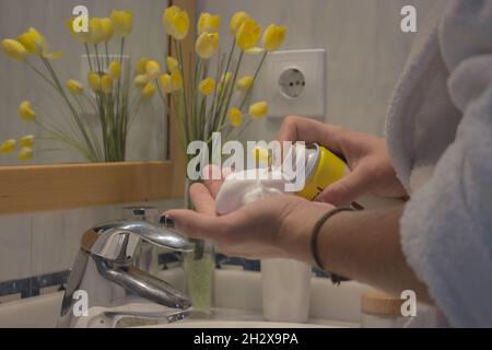 Gros plan jeune homme main dans le peignoir en ramassant la mousse de rasage dans la salle de bains de l'appartement.Concept de spa Beauty Home. Banque D'Images
