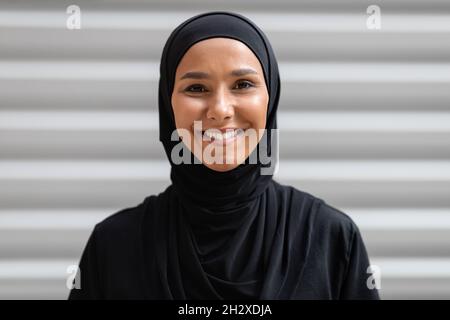 Portrait de jeune femme arabe souriante portant le hijab noir posant à l'extérieur Banque D'Images