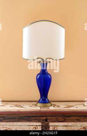 Lampe des années 50 avec support en verre bleu et abat-jour blanc placé sur une commode en bois contre un mur jaune dans la pièce Banque D'Images