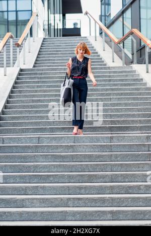 De dessous de corps de jeune femme moderne dans une tenue élégante avec sac marchant dans l'escalier dans la ville en été Banque D'Images