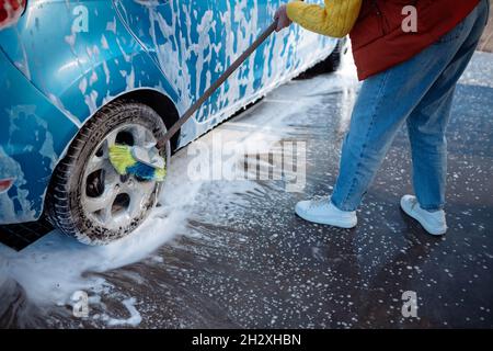 Belle jeune fille lave la voiture au lavage de voiture libre-service. Effacer la saleté à la voiture avec une brosse Banque D'Images