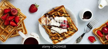 Gaufres belges carrées faites maison avec ricotta, chocolat, fraises et cerises pour le petit déjeuner sur fond de béton léger.Foyer sélectif Banque D'Images