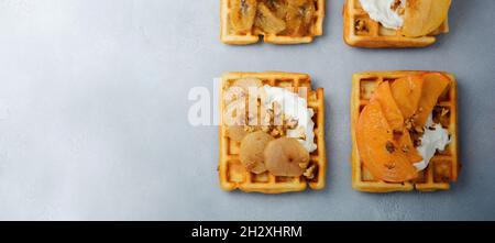 Délicieux gaufrettes belges avec fruits caramélisés, pomme, banane, persimmon, poire et noix sur fond de béton gris ou de pierre.Idées de breakfas Banque D'Images