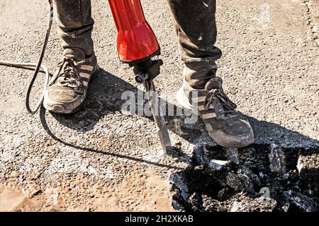 Un ouvrier répare la surface de la route avec un marteau à inertie le jour d'été.Travaux de construction sur la route. Banque D'Images