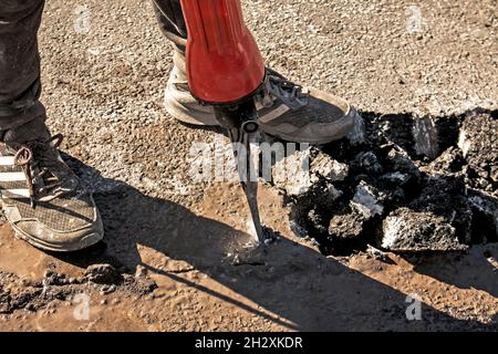 Un ouvrier répare la surface de la route avec un marteau à inertie le jour d'été.Travaux de construction sur la route. Banque D'Images