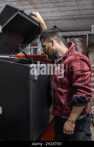 L'homme regardant dans une chaudière sur combustible solide dans la chambre avec des granulés. Banque D'Images