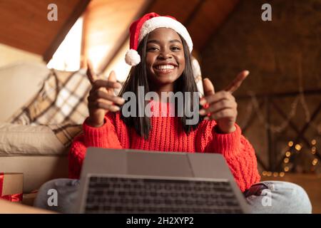 Bonne femme noire au chapeau de père Noël, passant des appels vidéo avec un ordinateur portable, saluant la famille avec Noël ou le nouvel an depuis la maison Banque D'Images