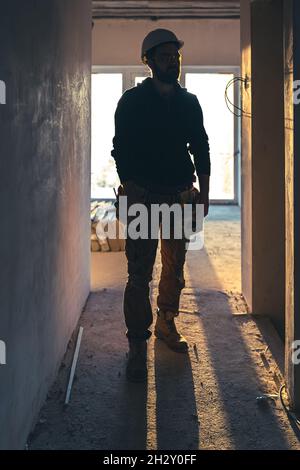 Un homme constructeur de vêtements de travail avec un casque de protection sur un chantier de construction. Banque D'Images