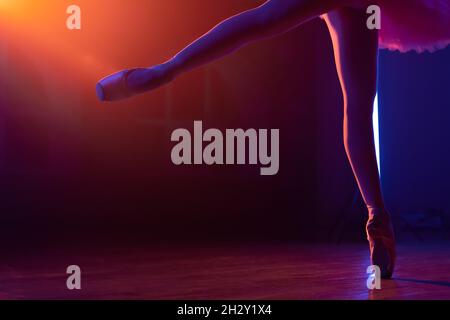 Les pieds de la danseuse de ballet, comment elle pratique en chaussures de pointe exercices sur fond de néon coloré, belles jambes de femme.Ballerines Banque D'Images