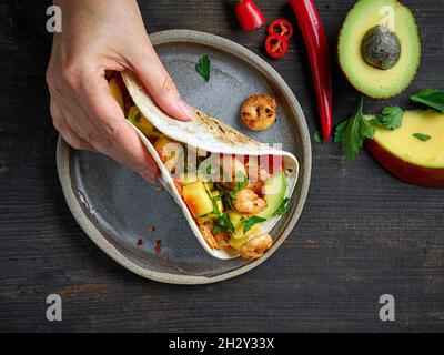Tacos de cuisine mexicaine à la main sur une table en bois sombre, vue du dessus Banque D'Images
