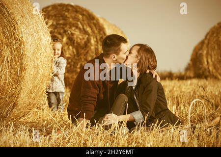 Une jeune famille heureuse avec une petite fille de deux ans à côté des balles de foin dans le champ récolté Banque D'Images