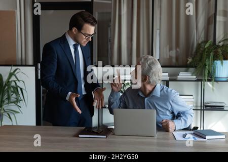 Un jeune homme agacé se disputent avec un collègue de la vieillesse nerveux Banque D'Images