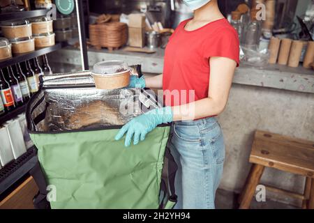 Femme travaillant dans un masque de protection pour le visage et enveloppant les aliments à l'intérieur Banque D'Images
