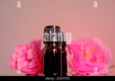 Huile essentielle de rose.Aromatherapy et concept de cosmétiques.Ensemble de bouteilles marron en verre et fleurs roses sur fond rose. Banque D'Images