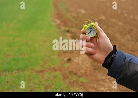 Temps d'ensemencement du printemps.Temps d'ensemencement..saison de travail dans les champs- Agriculture et agriculture.Le champ est vert et labouré et une main d'homme avec un réveil vert Banque D'Images