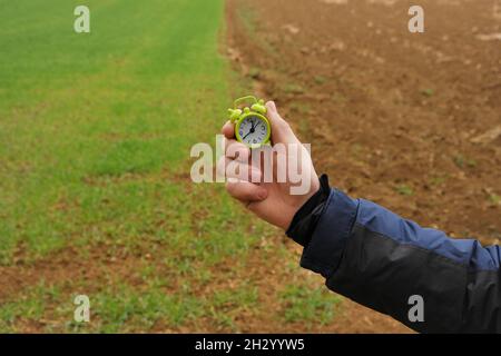 Temps d'ensemencement du printemps.Temps de semis.Agriculture et agriculture.Le champ est vert et labouré et une main d'homme avec un réveil.saison de travail de champ Banque D'Images