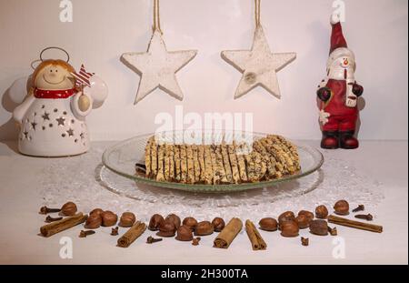 décor festif avec biscuits de noël faits maison sur une assiette en verre ; vue de face avec ornements décoratifs, épices et noisettes sur une table en bois blanc Banque D'Images