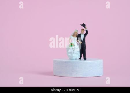 Concept de célébration de mariage miniature personnes, jouets photographie.Mariée et marié debout au-dessus de la plate-forme du podium isolé sur fond rose.Transfert d'image Banque D'Images