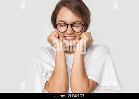 Jeune femme souriant à la caméra sur fond blanc.Portrait d'une fille portant des lunettes et tenant ses mains serrées dans des poings sur son puits Banque D'Images