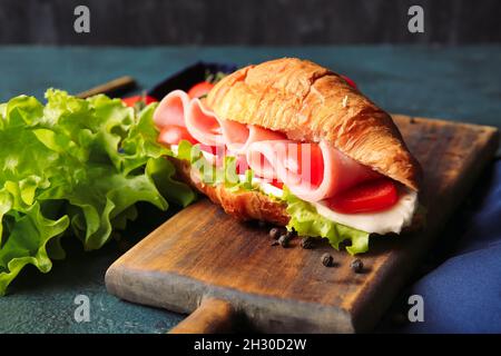 Planche en bois avec délicieux croissant sandwich sur fond noir Banque D'Images