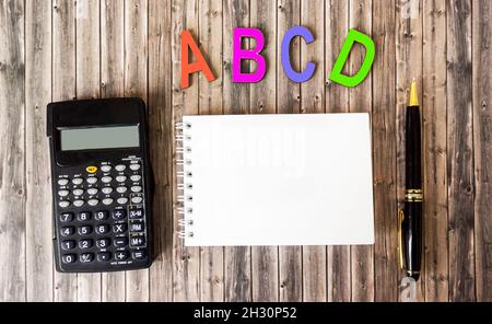 les lettres de l'alphabet de lettres de couleur bois se trouvent sur une table marron, à côté d'un bloc-notes pour l'écriture, d'une calculatrice et d'un stylo Banque D'Images