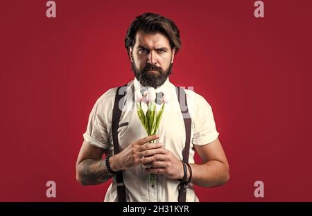 élégant homme brutal en tenue formelle a les cheveux soignés tenir des fleurs de tulipe, jour des femmes Banque D'Images