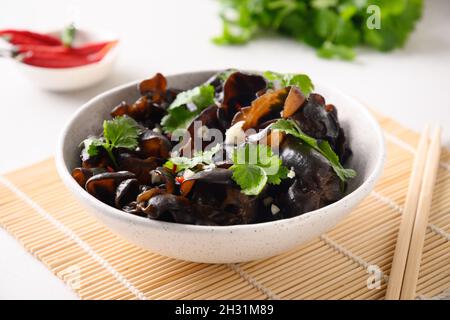 Salade de champignons noirs d'arbre marinés chinois avec piment et feuilles de coriandre dans un bol sur fond blanc.Gros plan. Banque D'Images