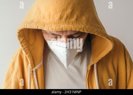 Homme décontracté avec une veste à capuchon jaune portant un masque respiratoire KN95 de protection pendant les pandémies Covid-19, foyer sélectif Banque D'Images