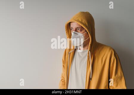 Homme décontracté avec une veste à capuchon jaune portant un masque respiratoire KN95 de protection pendant les pandémies Covid-19, foyer sélectif Banque D'Images