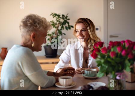 Bonne mère senior ayant un café avec une fille adulte à l'intérieur à la maison, assis et parlant. Banque D'Images