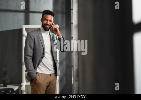 Un jeune homme d'affaires afro-américain heureux avec un téléphone fixe à l'intérieur au bureau, regardant la caméra. Banque D'Images