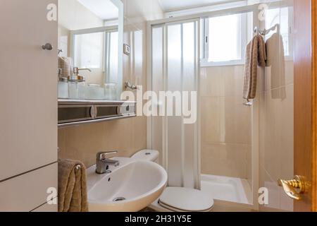 Intérieur de style simple de petite salle de bains avec murs en céramique beige, lavabo blanc, toilettes classiques et cabine de douche. Banque D'Images