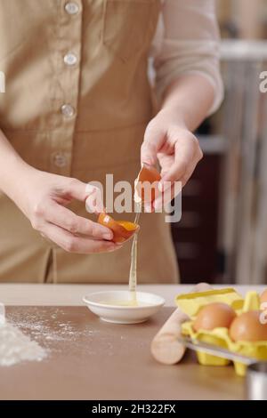 Processus de la jeune femme séparant le jaune d'œuf du blanc lors de la préparation de la pâte pour la pâtisserie Banque D'Images