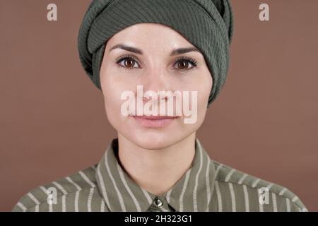 Visage d'une jeune femme musulmane contemporaine sérieuse en chemise rayée et coiffures regardant l'appareil photo Banque D'Images