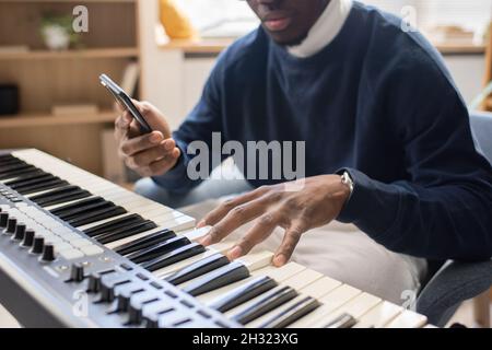 Jeune homme enseignant de musique avec smartphone touchant les touches du clavier de piano pendant la leçon en studio Banque D'Images