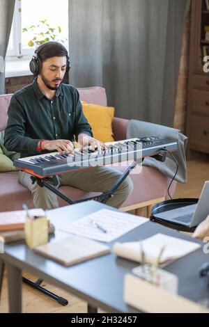 Jeune professeur de musique jouant le clavier de piano devant l'ordinateur portable pendant la leçon en ligne dans l'environnement à la maison Banque D'Images