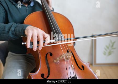 Main du jeune violoncelle qui glisse le violon sur les cordes tout en exécutant un morceau de musique devant l'appareil photo Banque D'Images