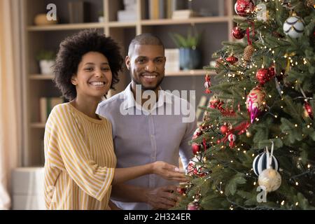 Portrait d'un couple afro-américain souriant posé près d'un arbre décoré. Banque D'Images