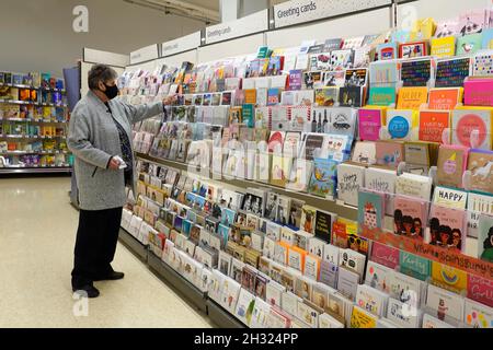 Femme mature senior magasiner dans un supermarché Sainsburys allée naviguer pour sélectionner un message sur un rack de cartes de vœux coloré Angleterre Royaume-Uni Banque D'Images