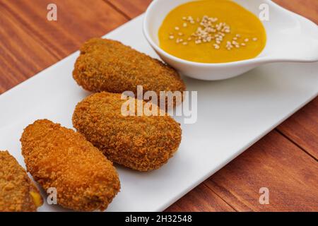 Croquettes frites avec sauce jaune sur plaque blanche.Vue latérale sur fond en bois. Banque D'Images