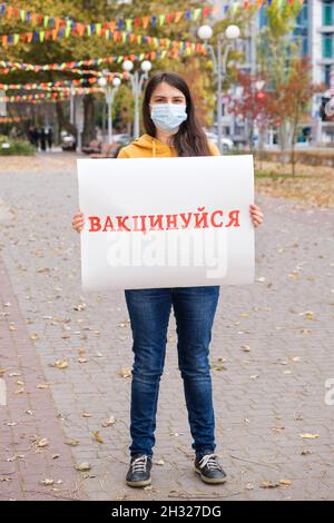 Une femme dans un masque médical tient une affiche avec une inscription, traduite de l'ukrainien se faire vacciner Banque D'Images