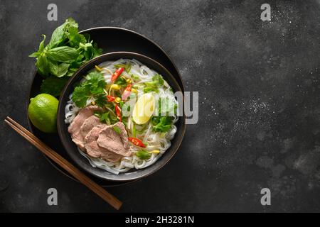 Soupe Pho Bo avec bœuf, nouilles de riz, gingembre, lime, piment dans un bol sur fond noir.Vue de dessus.Copier l'espace.Cuisine vietnamienne et asiatique Banque D'Images