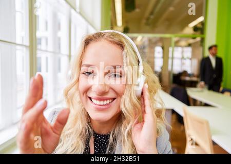 Jeune femme d'affaires joyeuse avec un casque agitant lors d'une vidéoconférence au bureau Banque D'Images