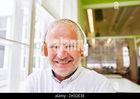 Un homme âgé avec casque sourit avec satisfaction tout en écoutant de la musique en streaming Banque D'Images