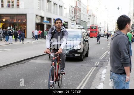 LONDRES, ANGLETERRE - octobre 19 2021 : un homme en manteau fait un vélo sur la route parmi les voitures Banque D'Images