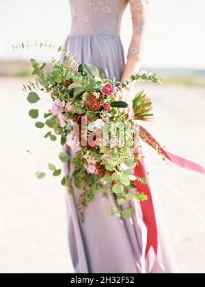 Grand bouquet de mariée violet moderne, gros plan.Belle mariée en violet robe de mariage se tient à la plage de sable.Bouquet de mariage énorme gros plan avec des ros Banque D'Images