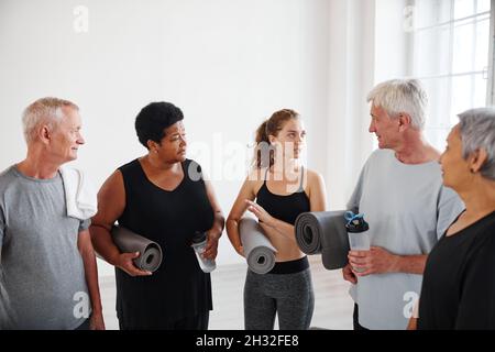 Groupe de personnes âgées avec tapis parlant à leur entraîneur après des cours de yoga dans le studio Banque D'Images