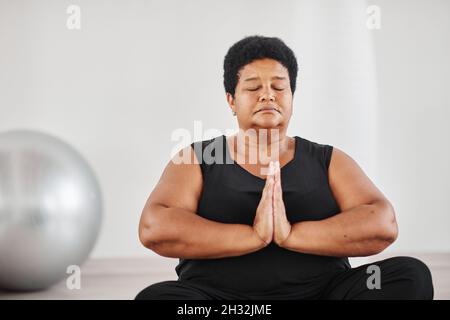 Portrait d'une femme africaine mûre assise en position lotus avec ses yeux fermés et méditant pendant le yoga Banque D'Images