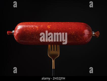 Saucisse fumée sur une fourchette sur fond noir. Banque D'Images